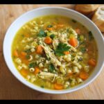 A close-up of a bowl of Lemon Chicken Immune Soup featuring shredded chicken, carrots, celery, and small pasta.