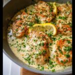 Close-up of seared chicken breasts simmering in a rich Lemon Garlic Cream Chicken Skillet sauce, garnished with parsley and lemon slices.