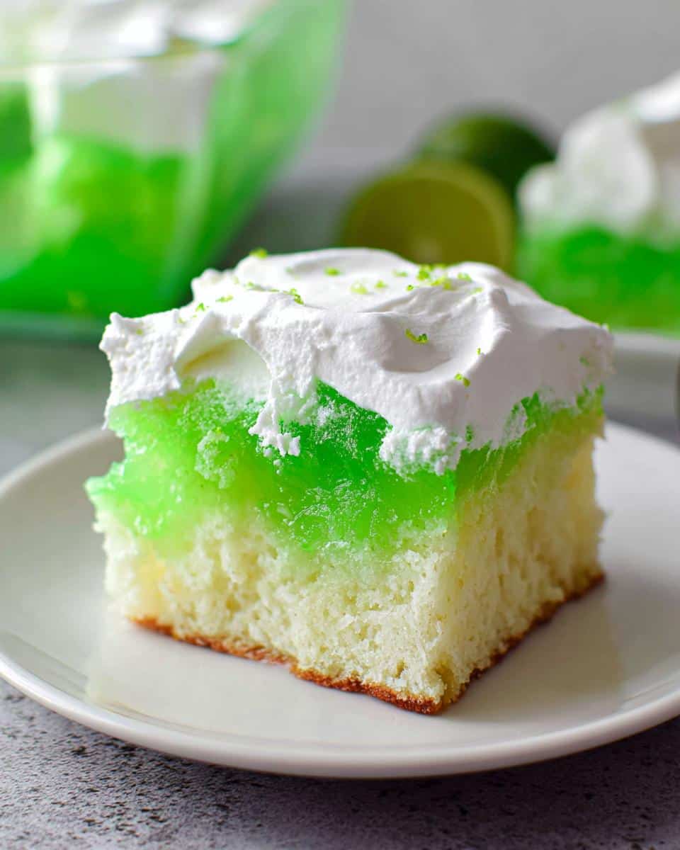 A square slice of bright green Lime Poke Cake topped with whipped cream and lime zest.