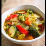 A close-up view of a hearty bowl of Low Calorie Vegetable Soup filled with broccoli, zucchini, cabbage, and red peppers.