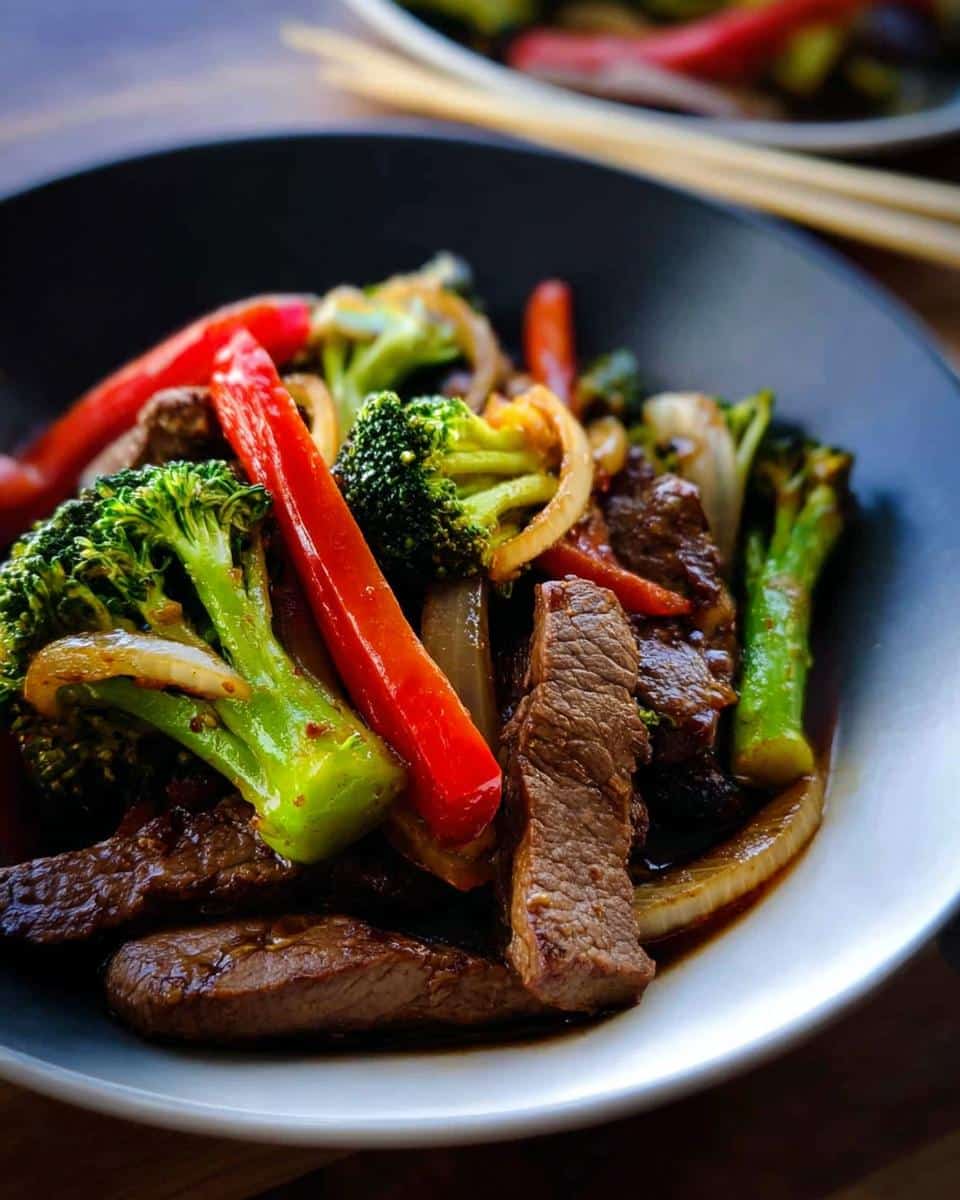 Close-up of vibrant Low Carb Beef Stir Fry featuring sliced beef, bright green broccoli, red peppers, and onions in a dark sauce.
