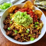 A close-up of a Low Carb Beef Taco Bowl featuring seasoned ground beef, cabbage, shredded cheese, a large dollop of guacamole, and salsa.