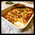 A portion removed from a baked Low Carb Chicken Parmesan Casserole topped with melted, browned cheese and fresh parsley.