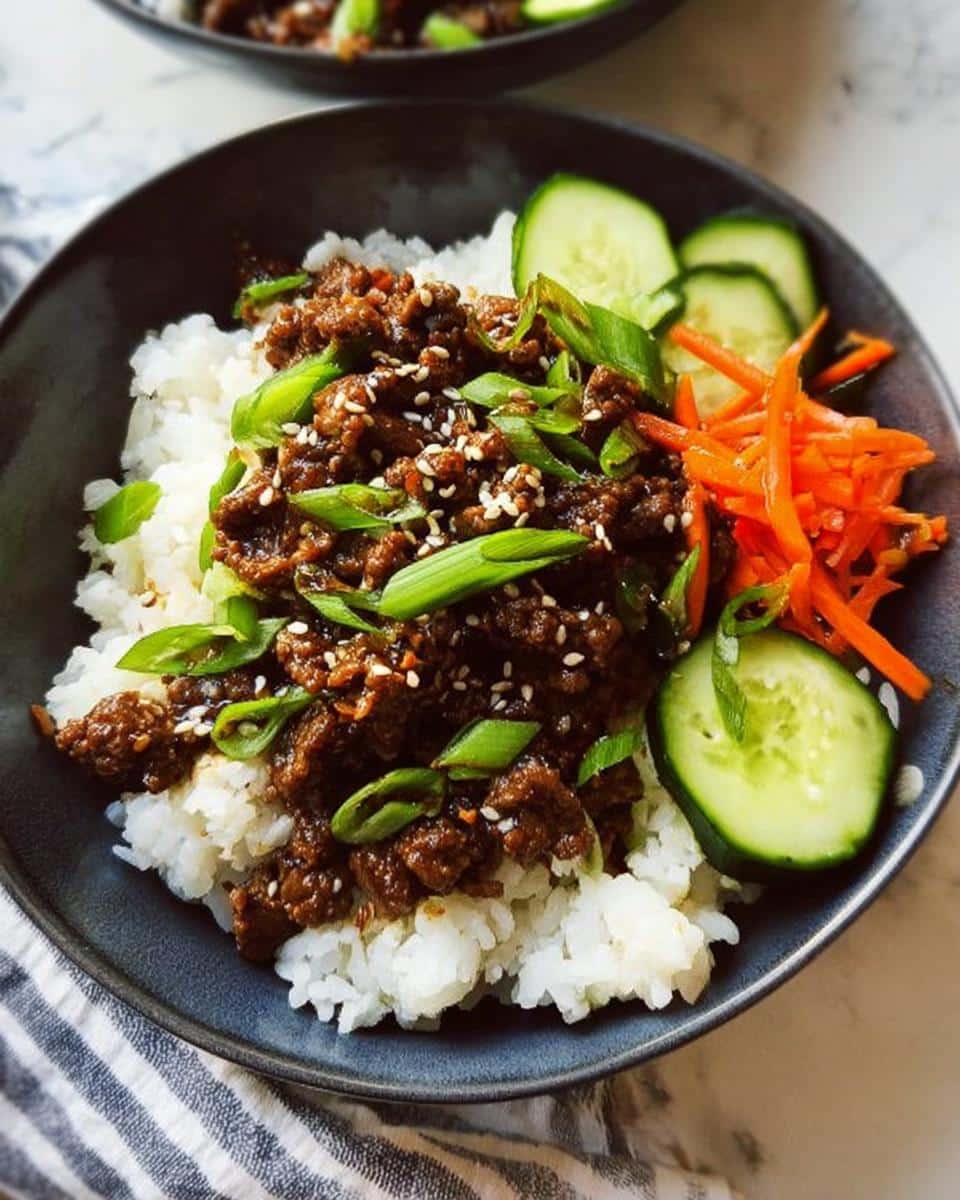 A close-up of a Low Carb Korean Beef Bowl featuring saucy ground beef over white rice, garnished with sesame seeds, scallions, cucumber, and shredded carrots.