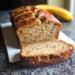 A loaf of moist Low Sugar Banana Bread, with one slice cut and resting against the main loaf.