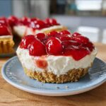 Close-up of a single Mardi Gras No-Bake Cheesecake Cup with a thick graham cracker crust and bright red cherry topping.