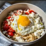 A bowl of Mediterranean Savory Overnight Oats topped with a sunny-side-up egg, feta cheese, and roasted tomatoes.