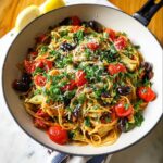 A skillet filled with vibrant Mediterranean Veggie Pasta, topped with roasted tomatoes, olives, parsley, and cheese.