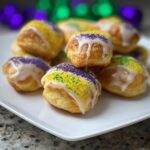 A pile of golden Mini King Cake Bites topped with white icing and purple, green, and yellow Mardi Gras sprinkles.