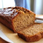Close-up of a freshly baked loaf of Allergy-Friendly Banana Bread, with one slice cut and resting beside it.