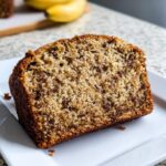 Close-up of a moist slice of Banana Bread With Yogurt showing chocolate chips and a golden crust.