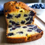 A close-up of moist Blueberry Banana Bread, sliced to show the dense crumb packed with blueberries.
