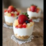 A close-up of a No-Bake Cheesecake Cup featuring a graham cracker crust, creamy filling, and topped with fresh strawberries and blueberries.