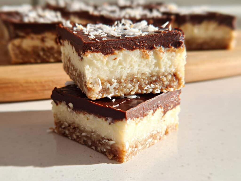 Two stacked squares of No-Bake Coconut Dessert Bars showing a crust, white coconut layer, and chocolate ganache topping.