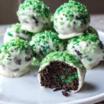 Close-up of a No-Bake Mint Oreo Truffles, cut open to show dark filling with green specks, dipped in white chocolate and topped with green sugar.