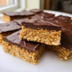 A stack of rich No-Bake Peanut Butter Oat Bars topped with a thick layer of melted chocolate.