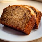 Close-up of two moist slices of Quick Banana Bread for Beginners with visible chocolate chips on a white plate.
