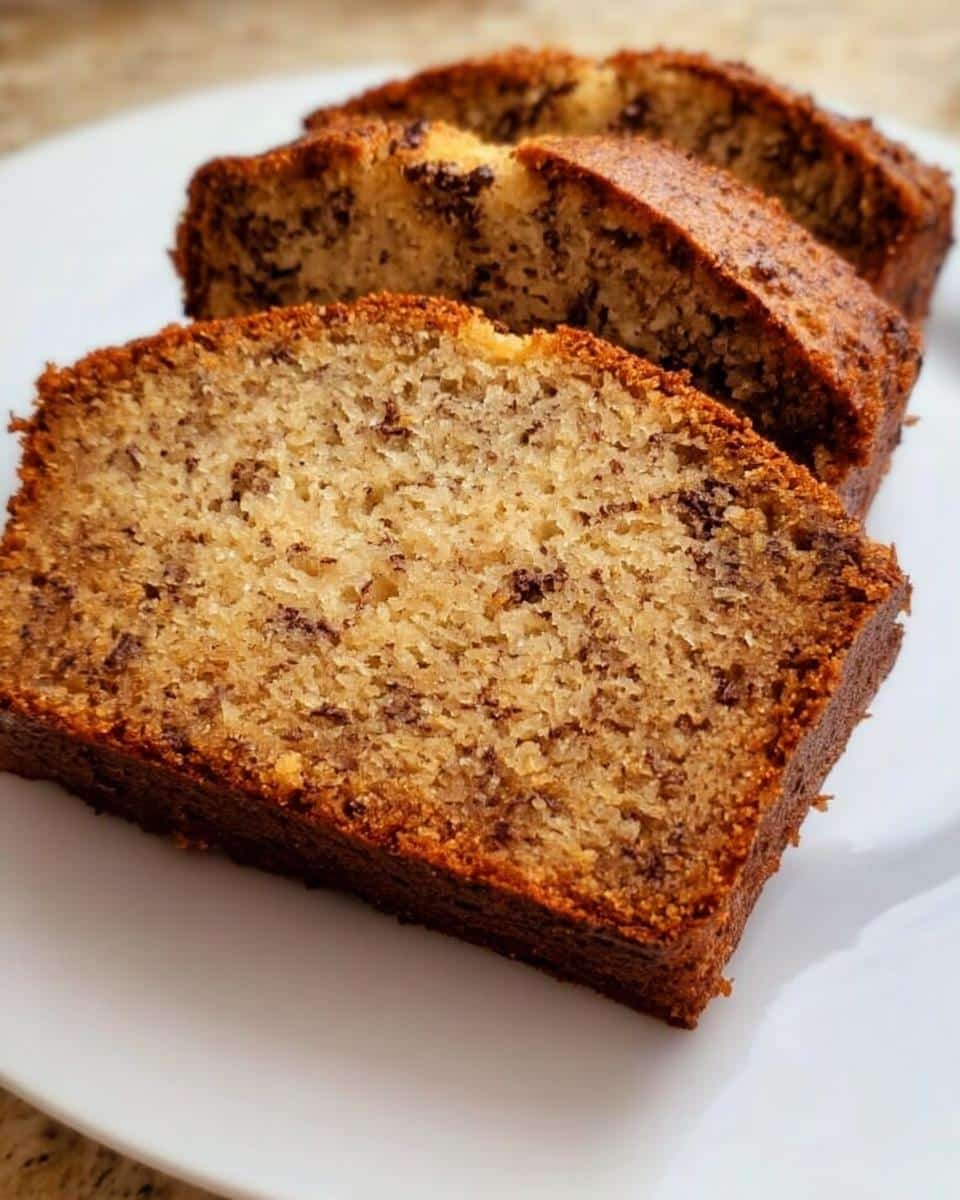 Three thick slices of moist Quick Banana Bread for Beginners, studded with chocolate chips, resting on a white plate.