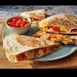 Four wedges of Quick Cheesy Chicken Quesadillas filled with shredded chicken, peppers, and melted cheese, served with salsa.