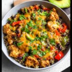 Close-up of a Santa Fe Chicken and Quinoa Bowl topped with melted cheese, black beans, peppers, and cilantro.