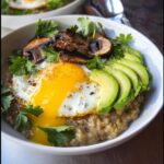 Close-up of Savory Oats with Avocado & Seeds topped with a sunny-side-up egg, sautéed mushrooms, and fresh parsley.