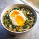 A bowl of Savory Overnight Oats with Egg & Spinach topped with a soft-boiled egg, spinach, and scallions.