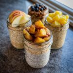 Four different jars of overnight oats meal prep jars, topped with fruit like apples, blueberries, and pineapple.