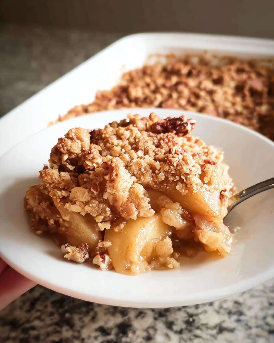 A spoonful of warm Gluten-Free Apple Crumble with a thick, nutty topping served on a white plate.