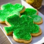 Close-up of several shamrock sugar cookies topped with bright green icing and sparkling green sprinkles.