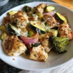 Melted cheese topping pieces of seasoned chicken and roasted zucchini, onion, and broccoli from Sheet Pan Chicken and Veggies (Low Carb).
