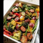 A close-up of Sheet Pan Sausage and Vegetables, including sausage slices, red potatoes, broccoli, and green beans, roasted together.