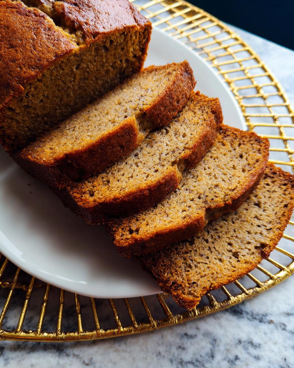 Slices of moist Vegan Banana Bread Without Butter displayed on a white plate with a gold wire mat underneath.