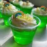 Close-up of bright green St. Patrick’s Day Jello Shots topped with whipped cream, gold sprinkles, and a rainbow candy.