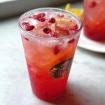 Close-up of a bright red and pink Starbucks Lemonade Refresher DIY, filled with ice and topped with dried berries.