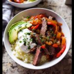 Close-up of a Steak Fajita Low Carb Bowl featuring sliced steak, peppers, cauliflower rice, avocado, and sour cream.