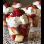 A close-up of one serving of Strawberry Shortcake Trifle Cups layered with cake, macerated strawberries, and whipped cream, topped with a whole strawberry.