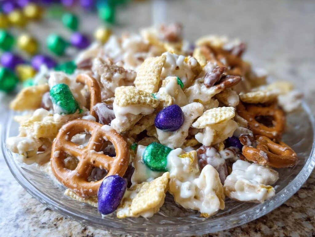 Close-up of sweet Mardi Gras Snack Mix featuring pretzels, cereal coated in white chocolate, and purple and green candies.