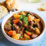 A close-up of a bowl filled with rich, Thick Beef Stew featuring tender beef chunks, potatoes, and carrots, garnished with rosemary.