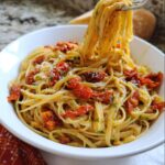 A fork lifting linguine from a bowl of Valentine Pasta with Roasted Tomatoes, topped with Parmesan.