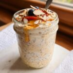 Close-up of Vanilla Almond Overnight Oats topped with sliced almonds, berries, and drizzled with honey.
