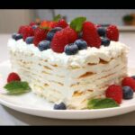 A layered Vanilla Wafer Icebox Cake topped with whipped cream, fresh raspberries, and blueberries.