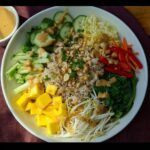 Overhead view of a colorful Gluten-Free Buddha Bowl featuring rice, mango, cucumber, sprouts, and peanut dressing.