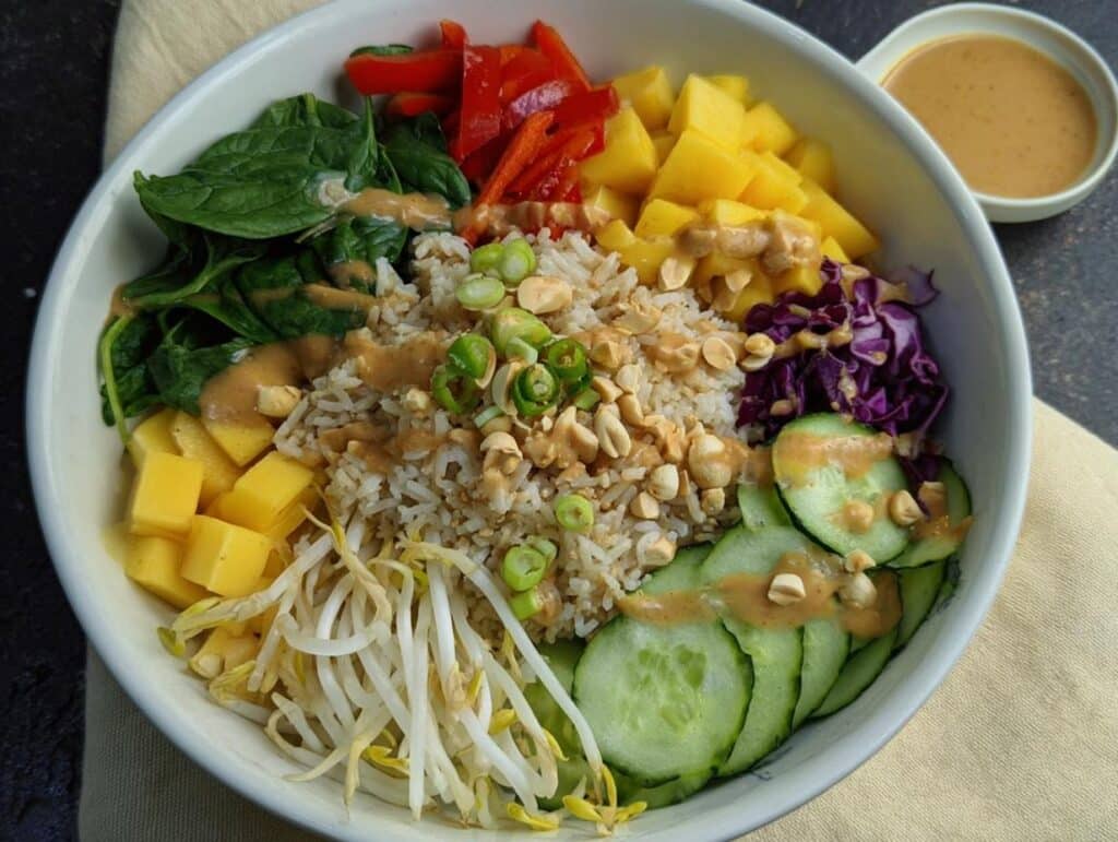 Overhead view of a colorful Gluten-Free Buddha Bowl featuring rice, mango, spinach, cucumber, and peanut dressing.