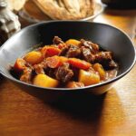 Close-up of rich Winter Beef Stew with chunks of beef, carrots, and potatoes in a dark bowl.